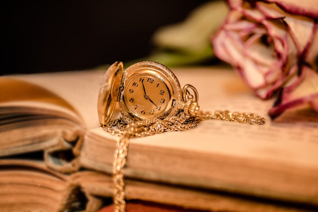本の上に金の鎖の付いた時計とバラが置かれている写真