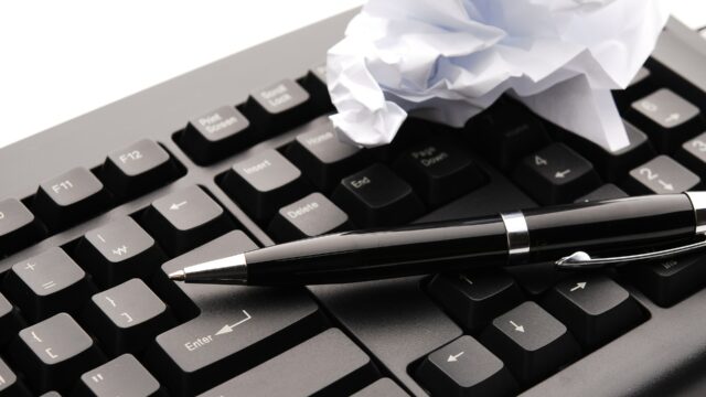 黒いパソコンのキーボードとペンと丸められた紙の写真